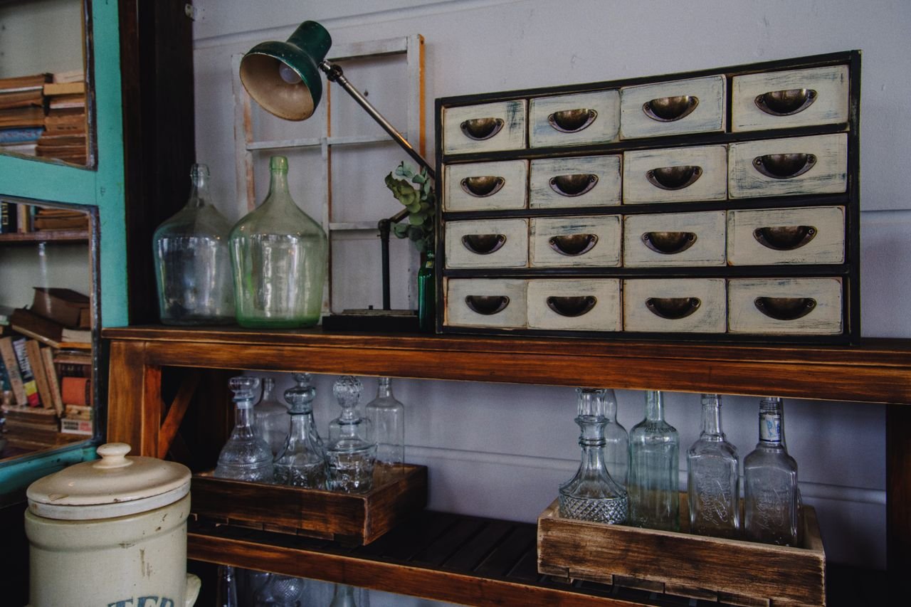 services-02 A rustic indoor scene featuring a vintage cabinet and glass bottles on a wooden shelf.